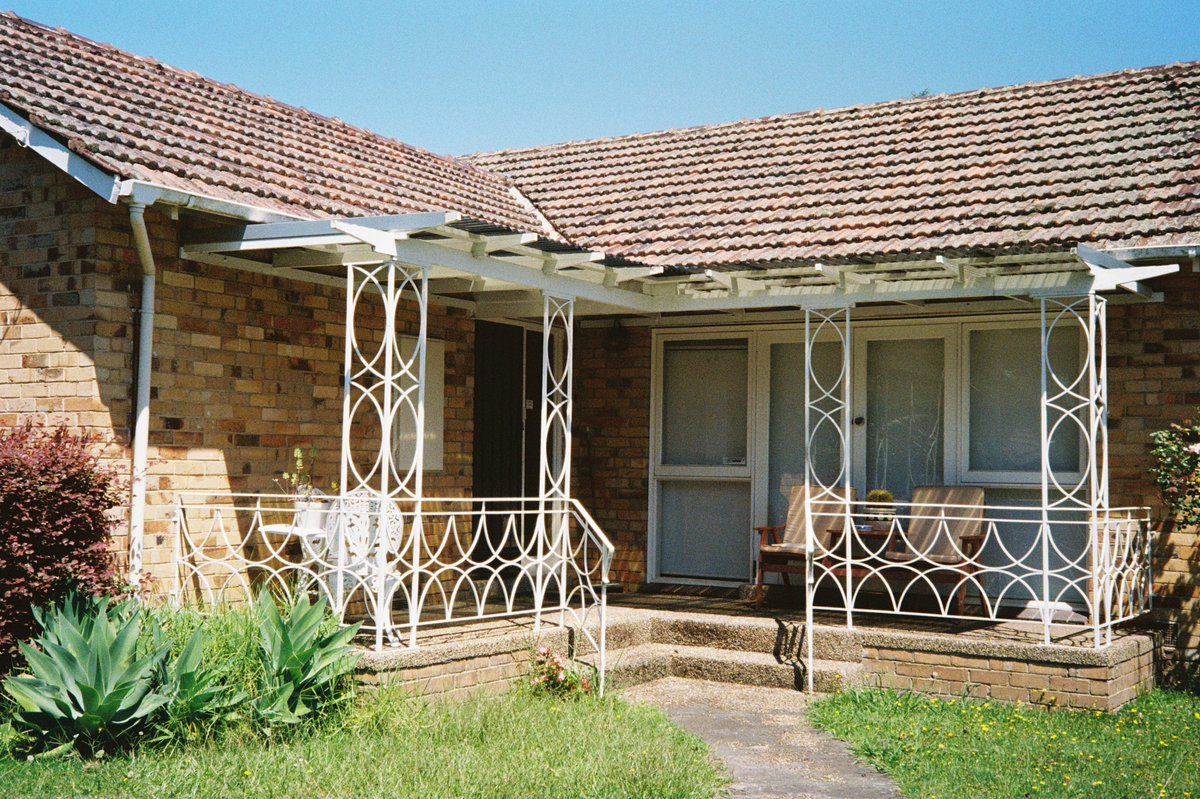 Alex Lahey's Garage Days EP cover features a suburban brick house with white decorative iron railings and a tiled roof.